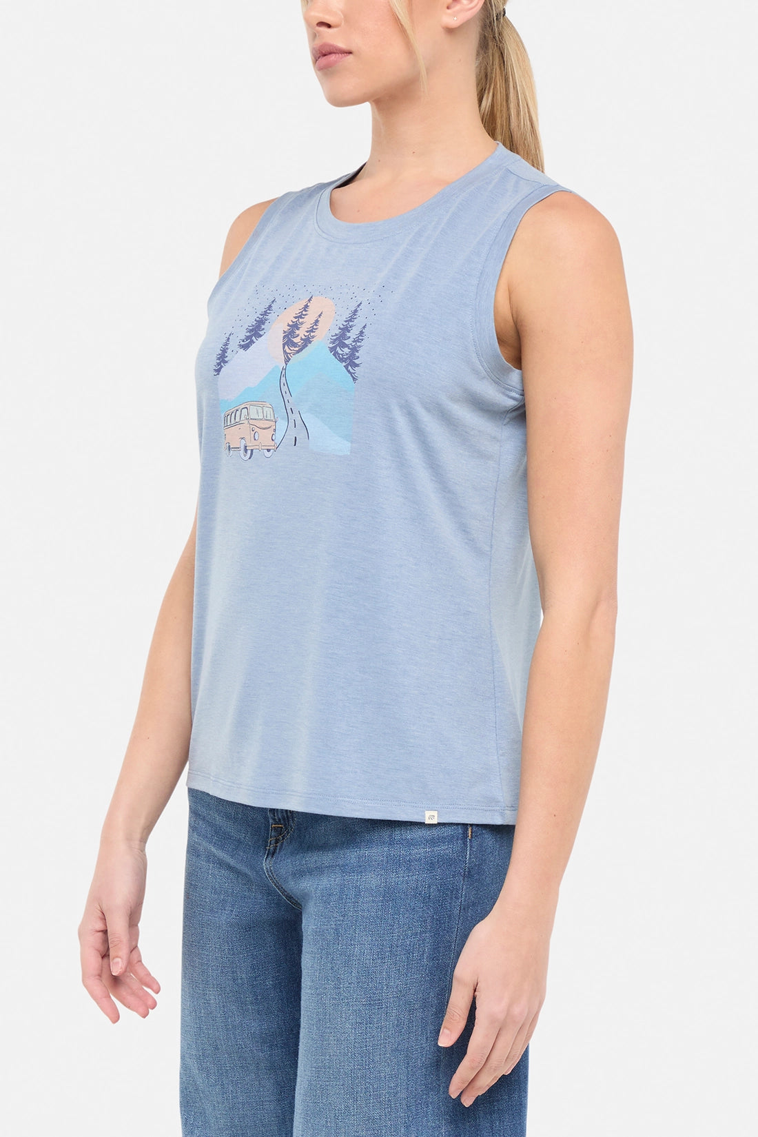 Side view of woman wearing a sleeveless light blue shirt with a graphic design of a van and mountains on white background.