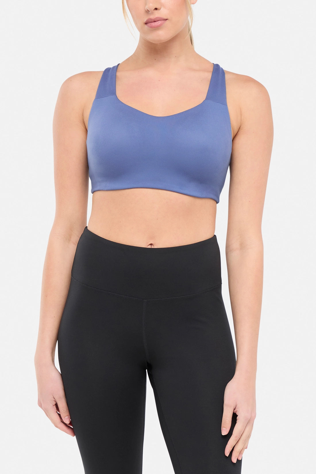 Front view of woman wearing a blue sports bra and black leggings on a white background.