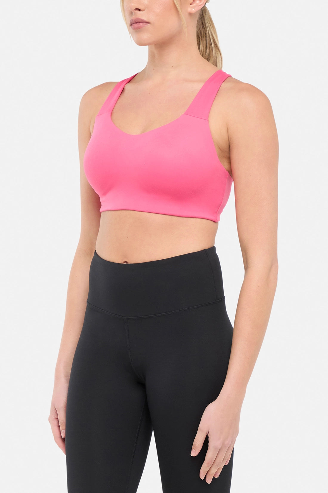 Side view of woman wearing a pink sports bra and black leggings on a white background.