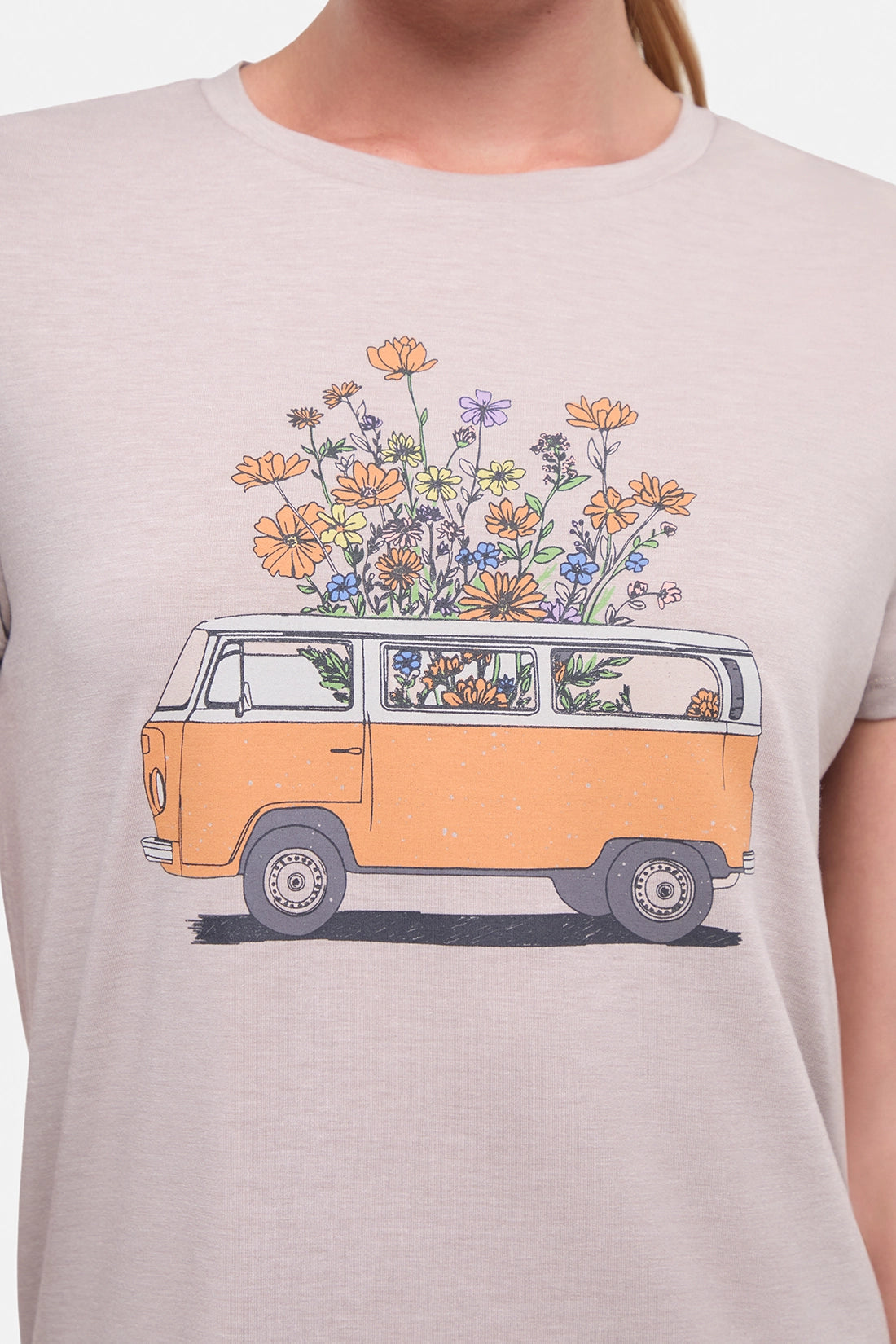 Close up front view of woman wearing a beige t-shirt with a graphic of an orange van and flowers on a .white background.