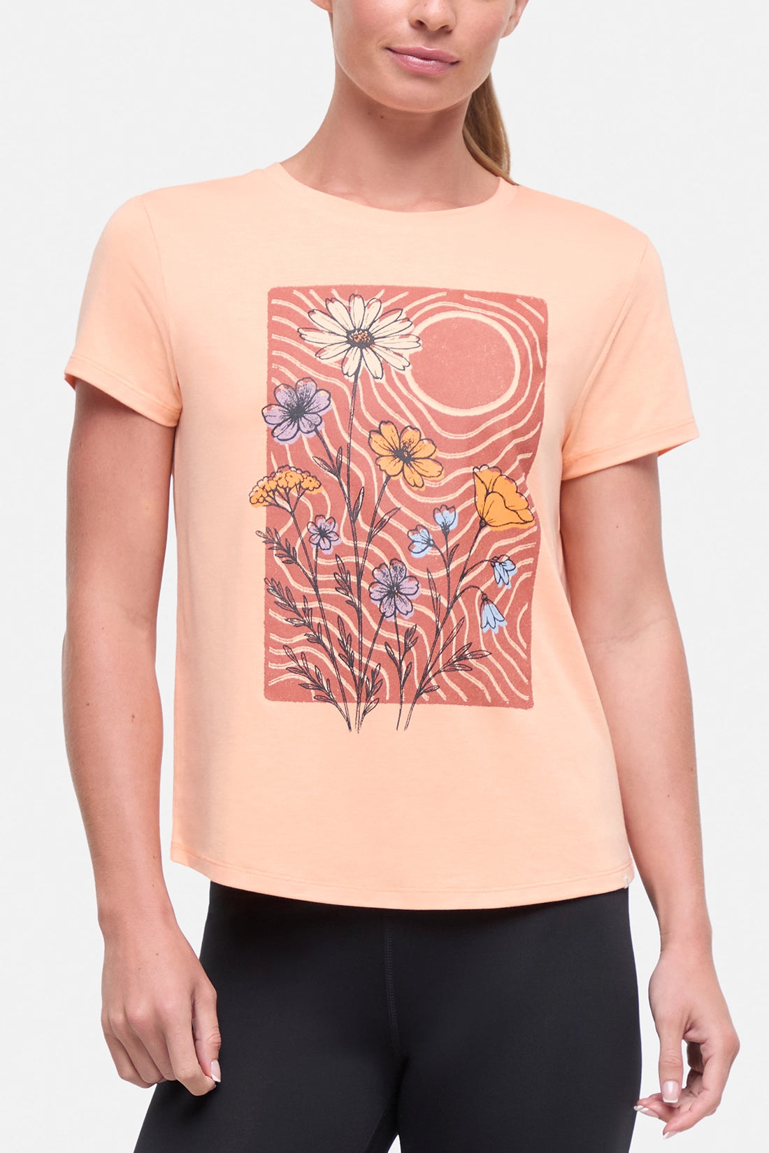 Front view of woman wearing a peach t-shirt with floral graphic on a light gray background.