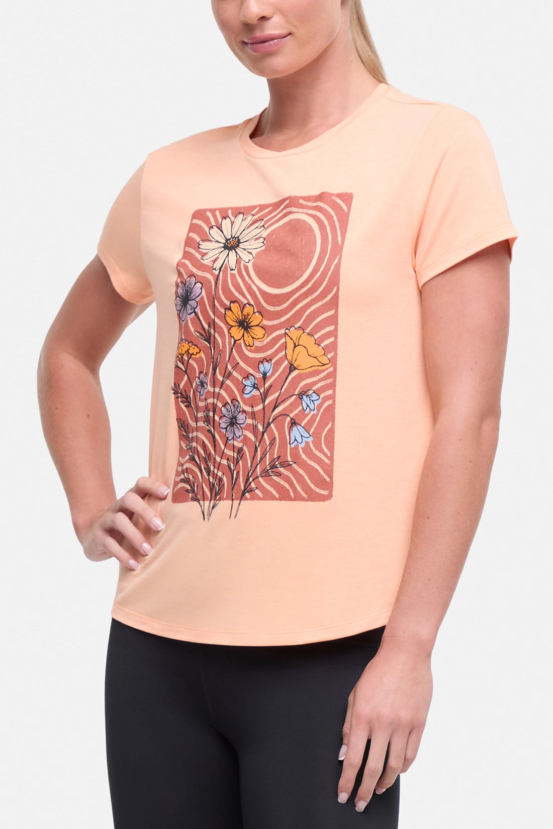 Front view of woman wearing a peach t-shirt with floral graphic on a light gray background.