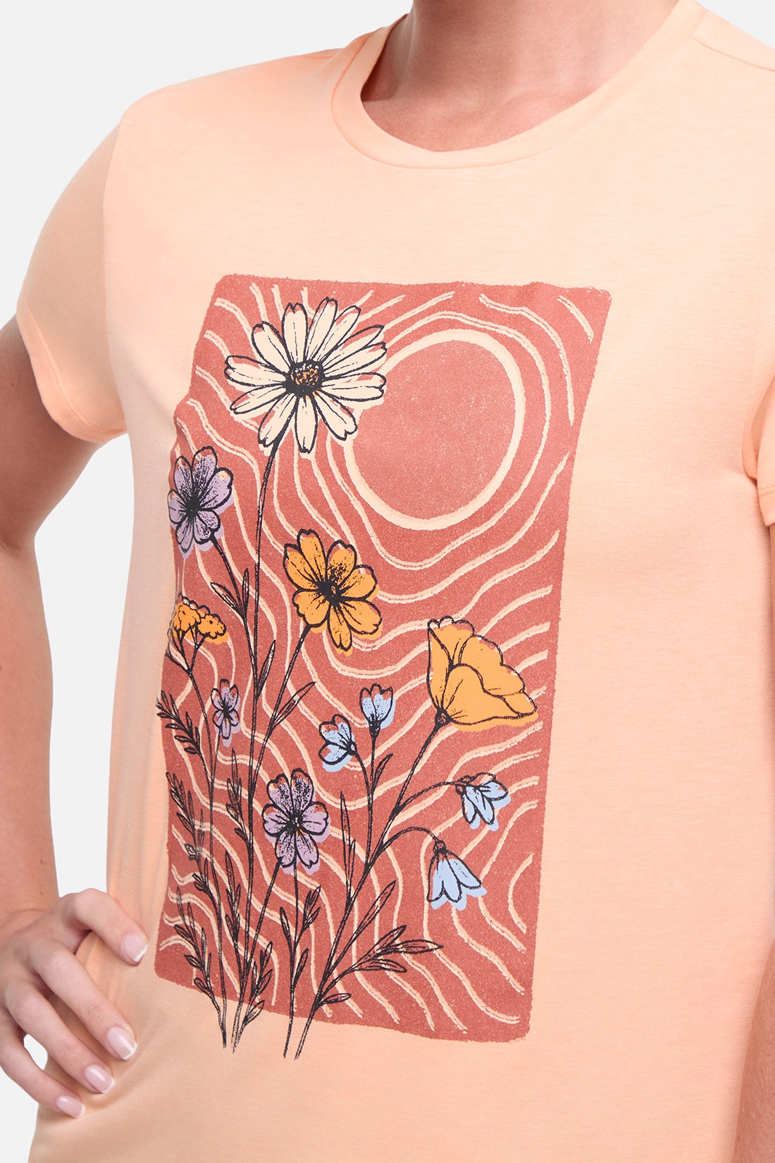 Close up front view of woman wearing a peach t-shirt with floral graphic on a light gray background.