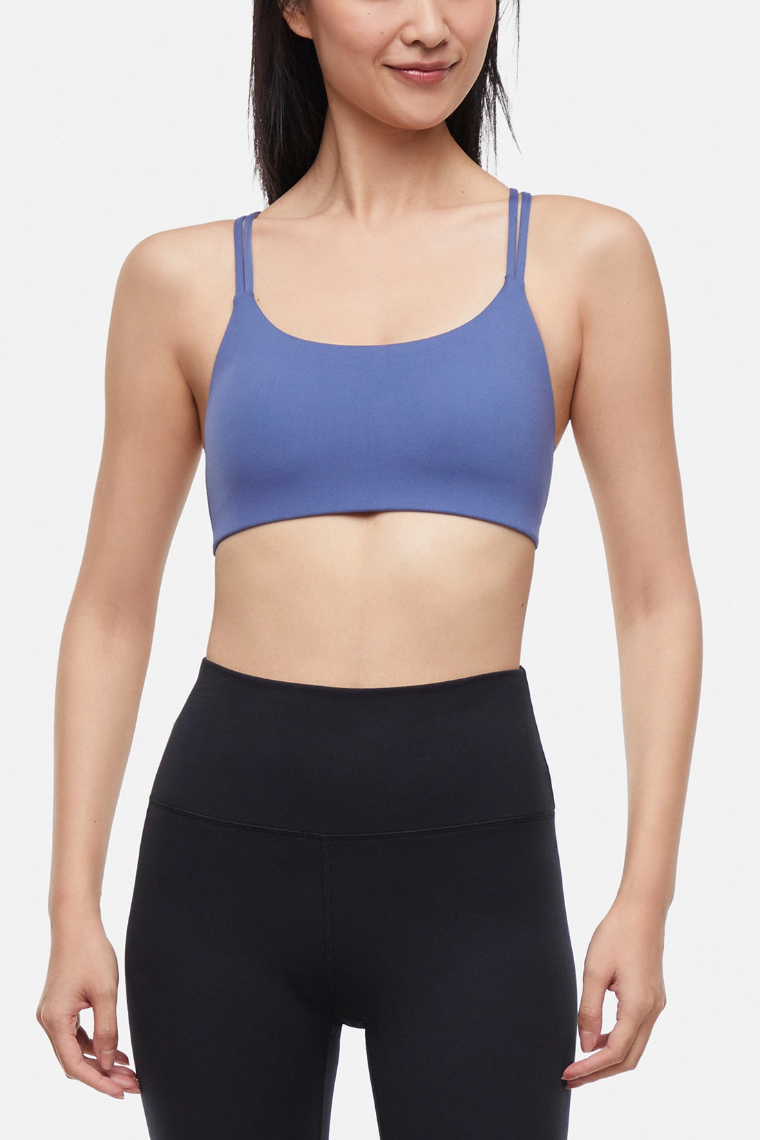 Front view of woman wearing a blue sports bra and black leggings on a white background.