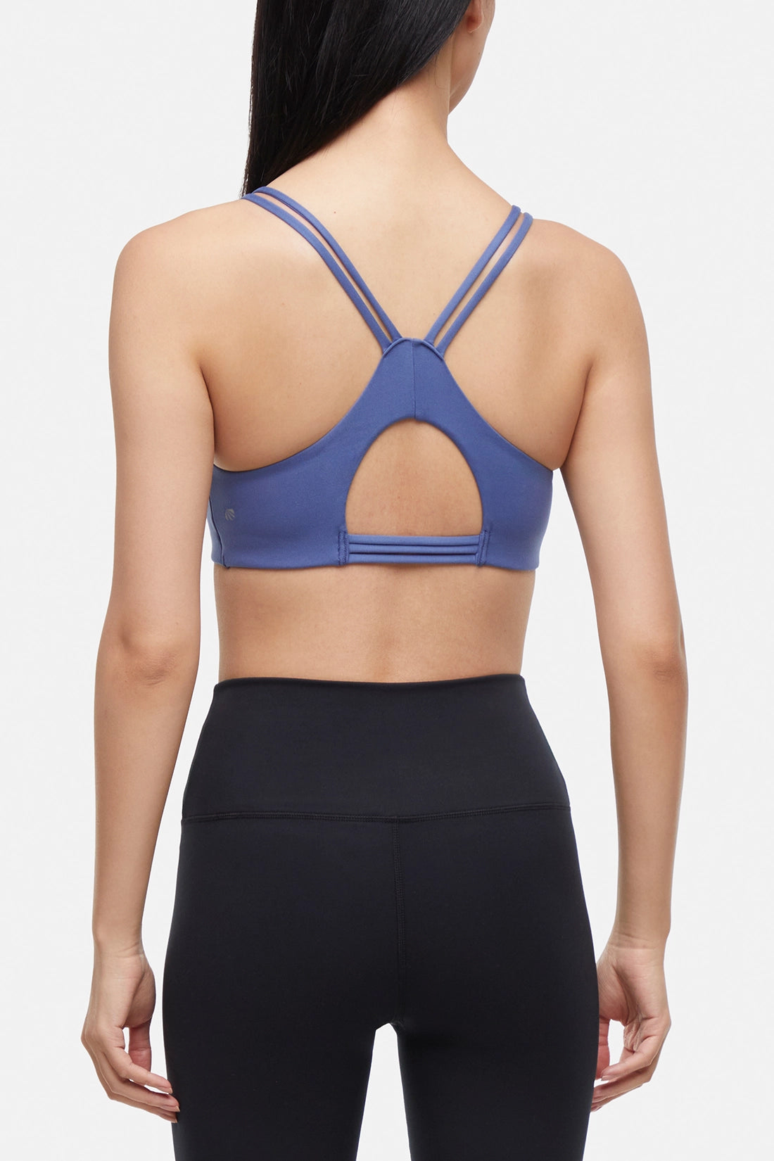 Back view of blue sports bra with crisscross straps and keyhole cutout detail on a plain background.
