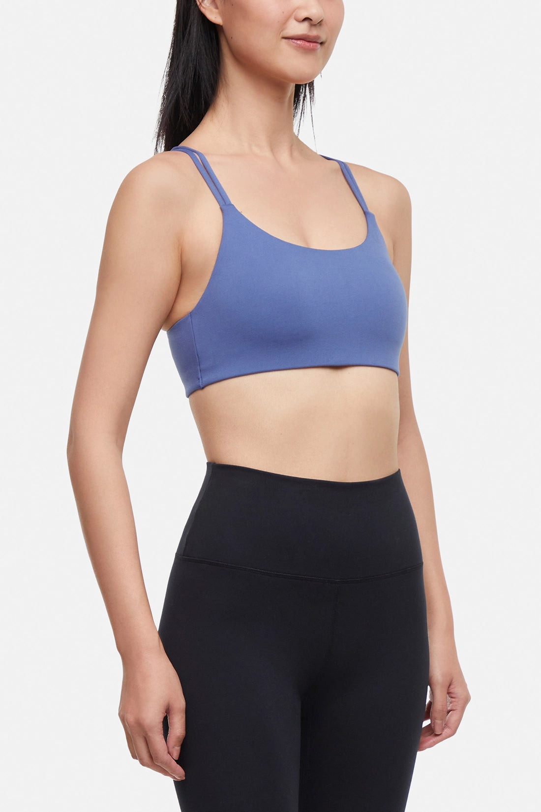 Front view of woman wearing a blue sports bra and black leggings on a white background.