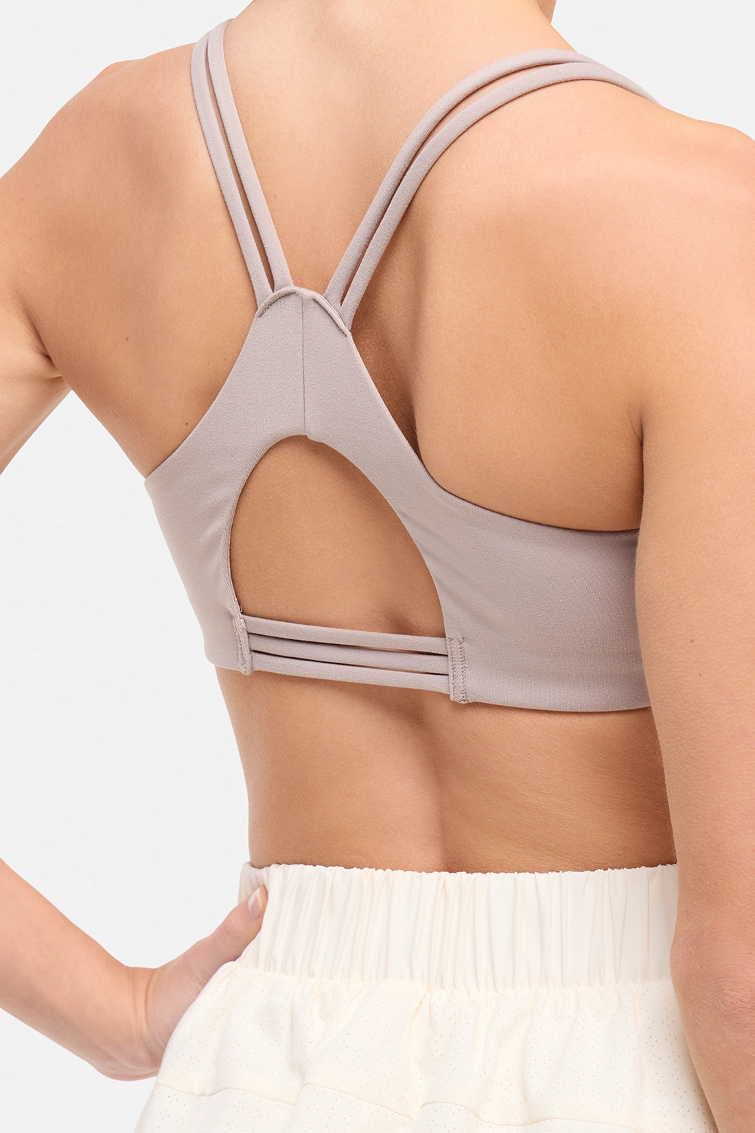 Back view of woman wearing a light grey-beige sports bra and white skort on a white background.