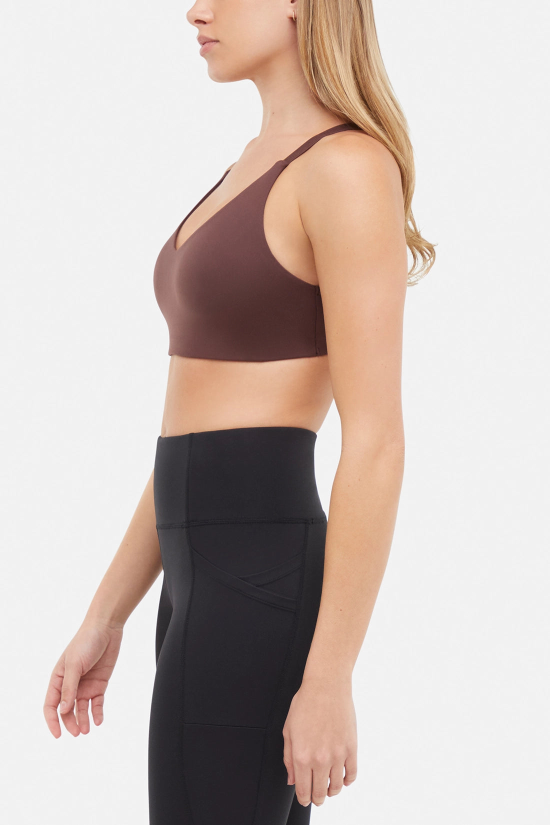 Side view of woman wearing a brown sports bra and black leggings on a white background.