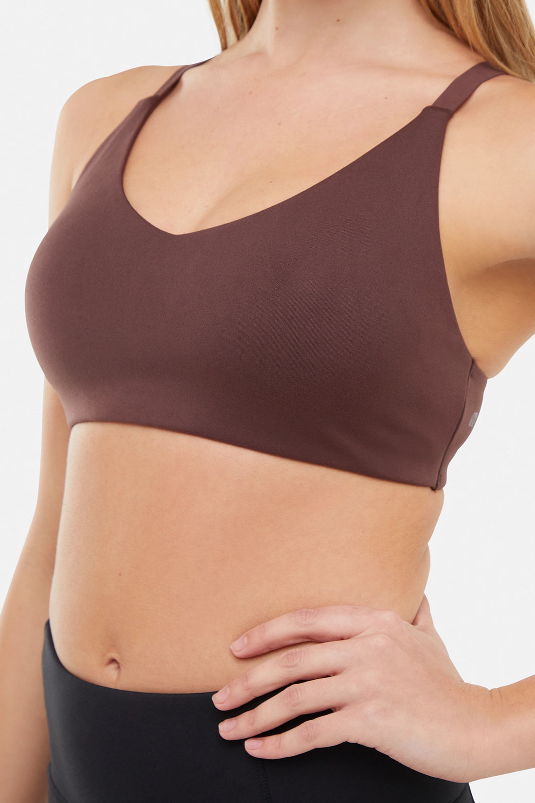 Close up front view of woman wearing a brown sports bra and black leggings on a white background.