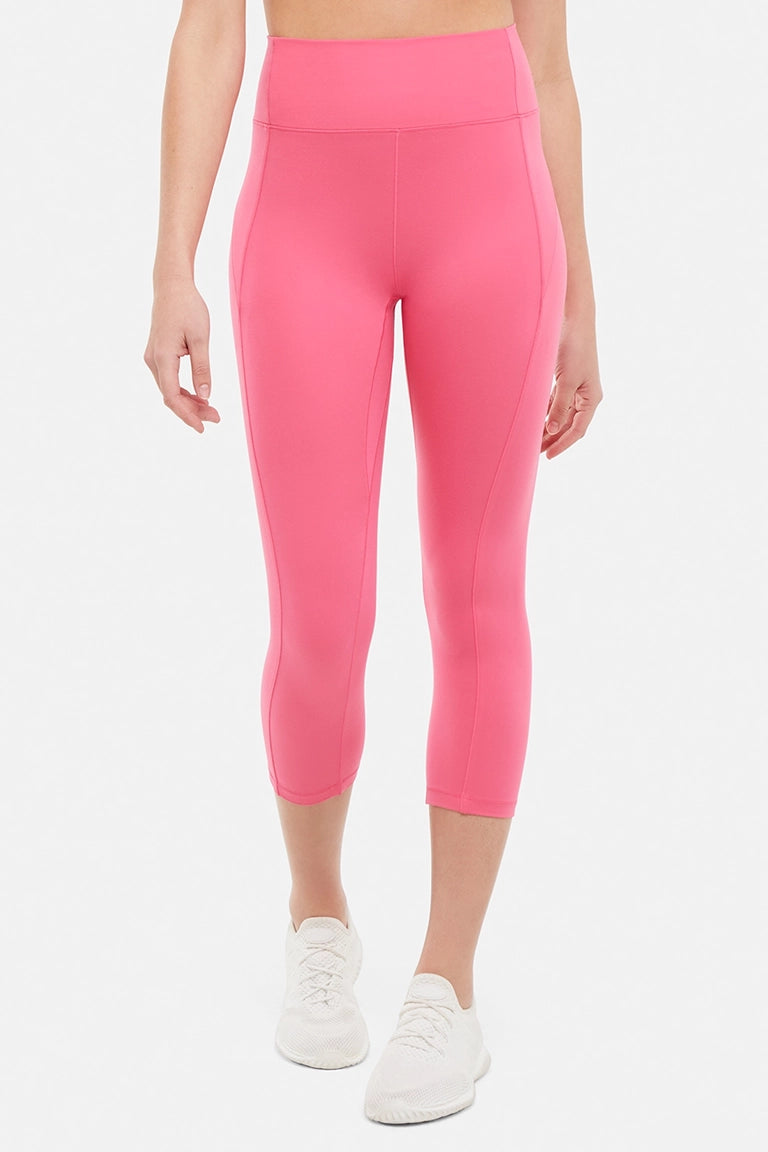 Front view of woman wearing pink capris and white sneakers on a light gray background.