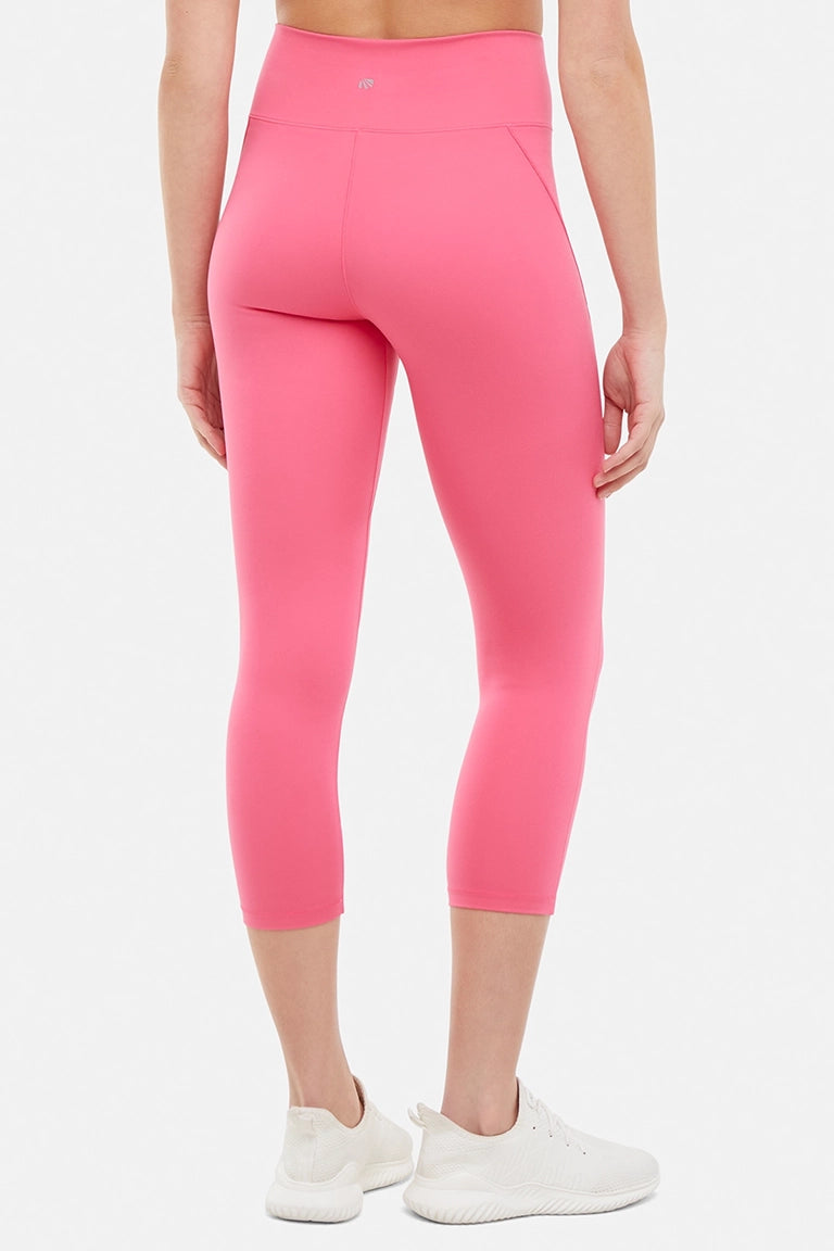 Back view of woman wearing pink capris and white sneakers on a light gray background.