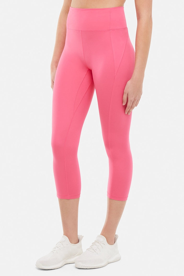 Front view of woman wearing pink capris and white sneakers on a light gray background.