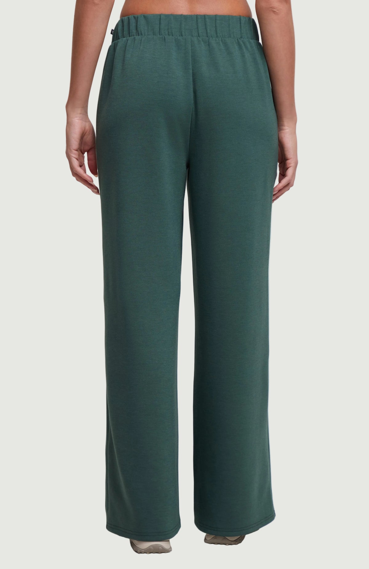 A person shown from the back wearing dark teal wide-leg lounge pants against a plain grey studio background.