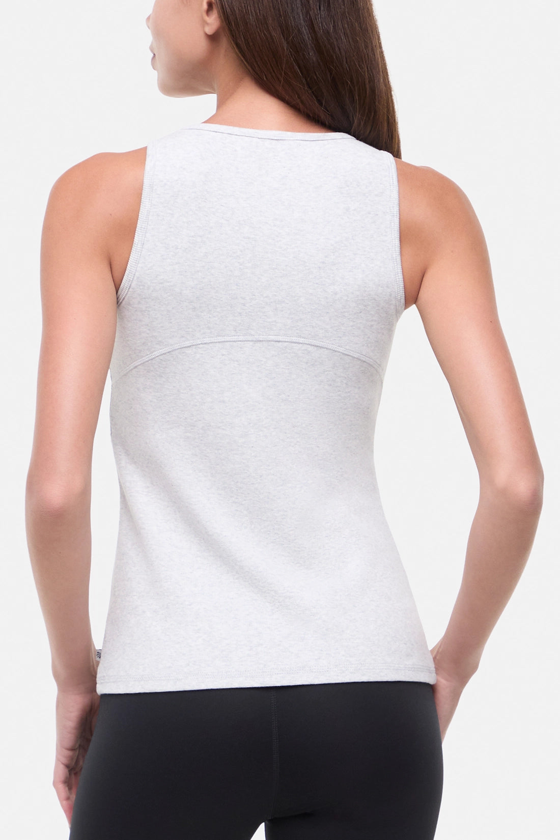 Back view of woman wearing a heather gray sleeveless tank top and black leggings on a light gray background.