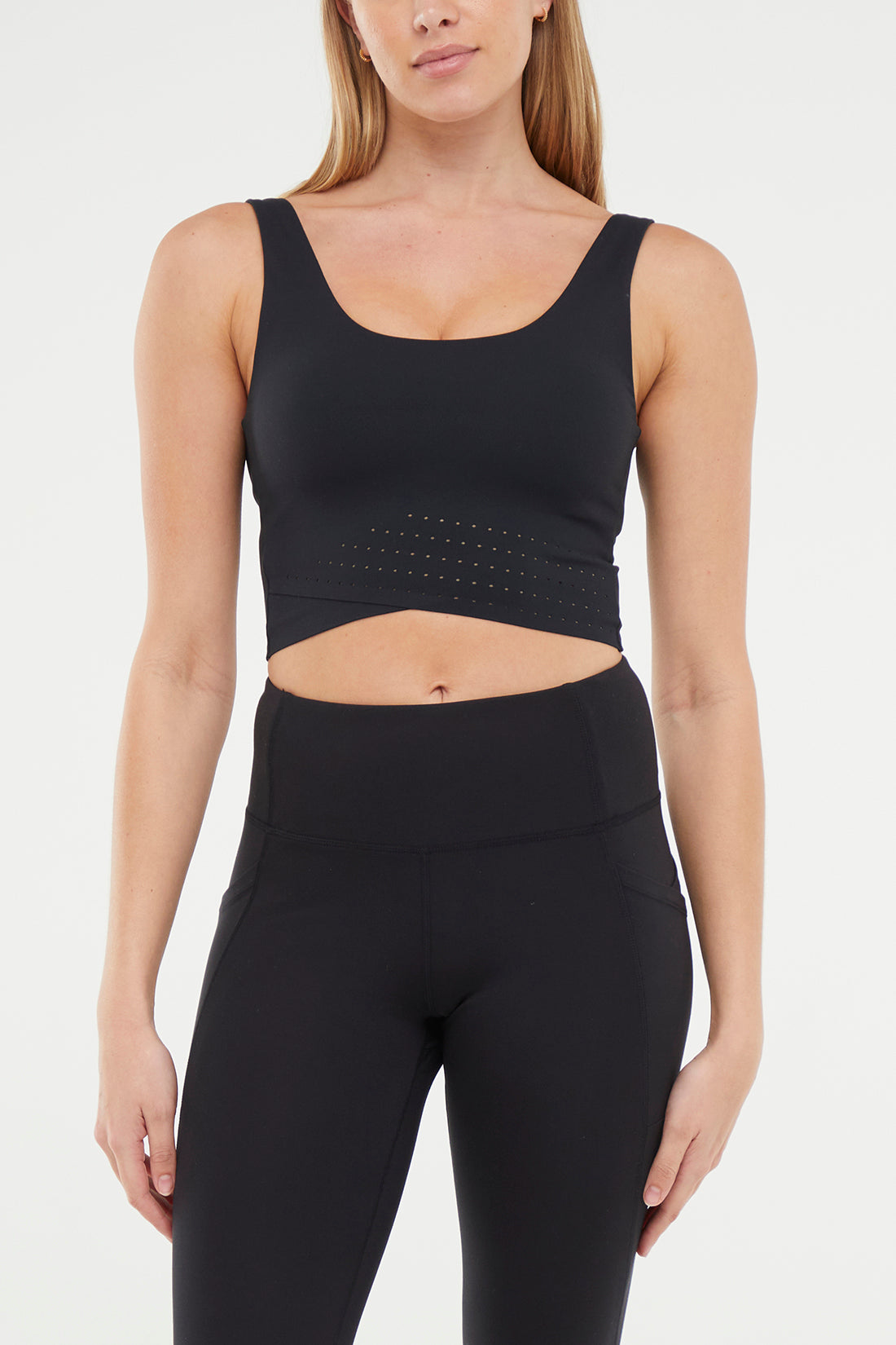 Front view of woman wearing a black sports bra and black leggings on a white background.