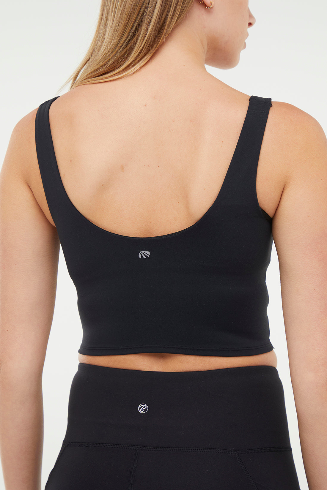 Back view of woman wearing a black sports bra and black leggings on a white background.