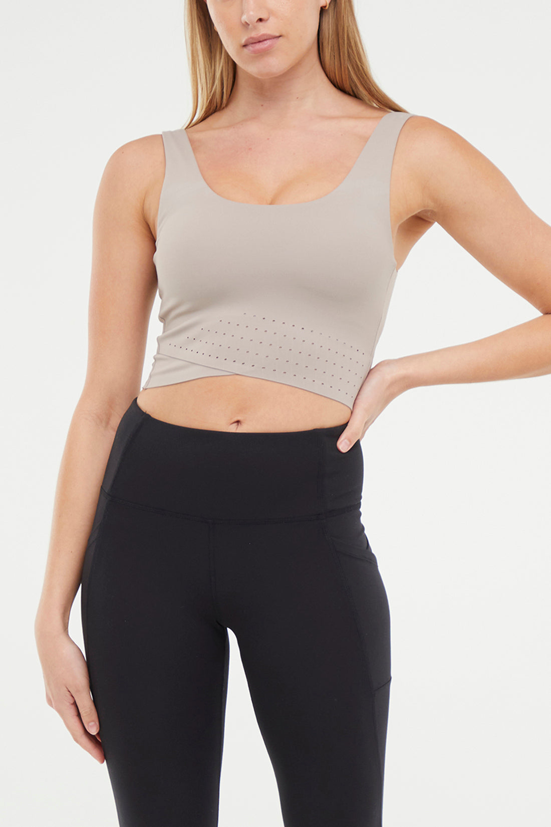 Front view of woman wearing a beige sports bra and black leggings on a white background.