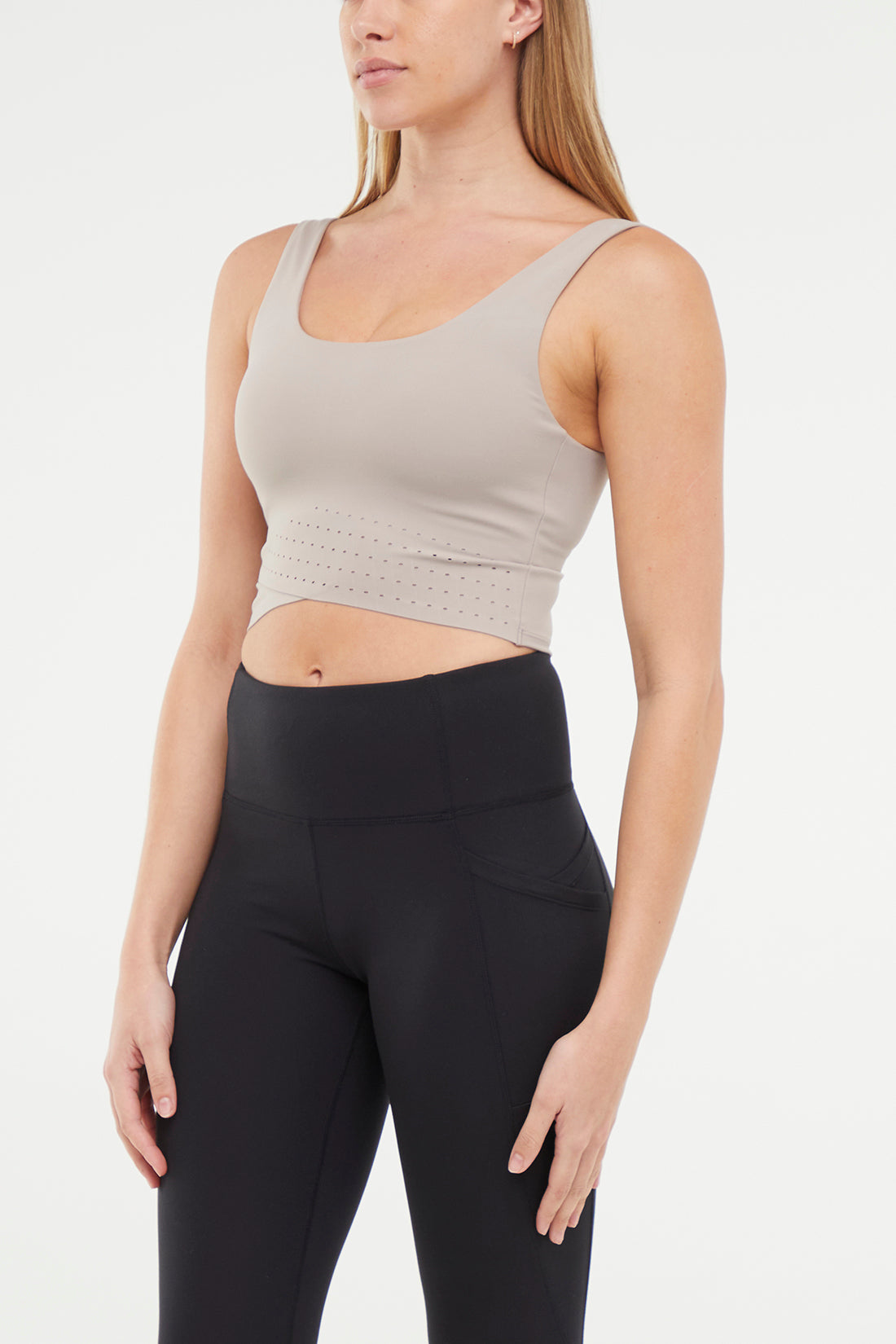 Quarter view of woman wearing a beige sports bra and black leggings on a white background.