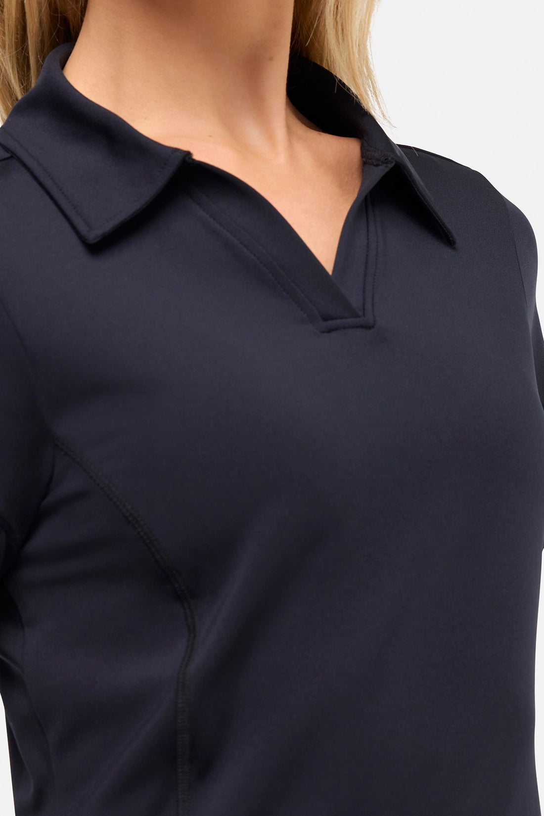 Close up front view of woman wearing a black polo shirt and black pants on a white background.