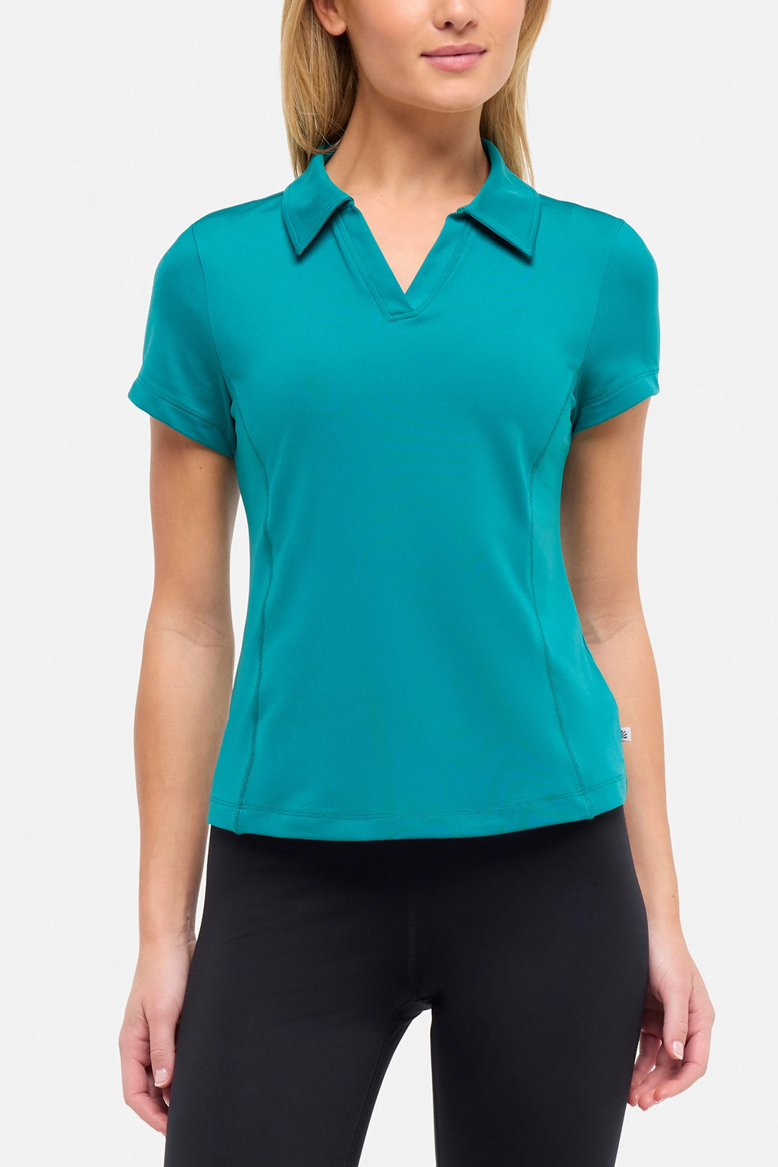 Front view of woman wearing a teal polo shirt and black pants on a white background.