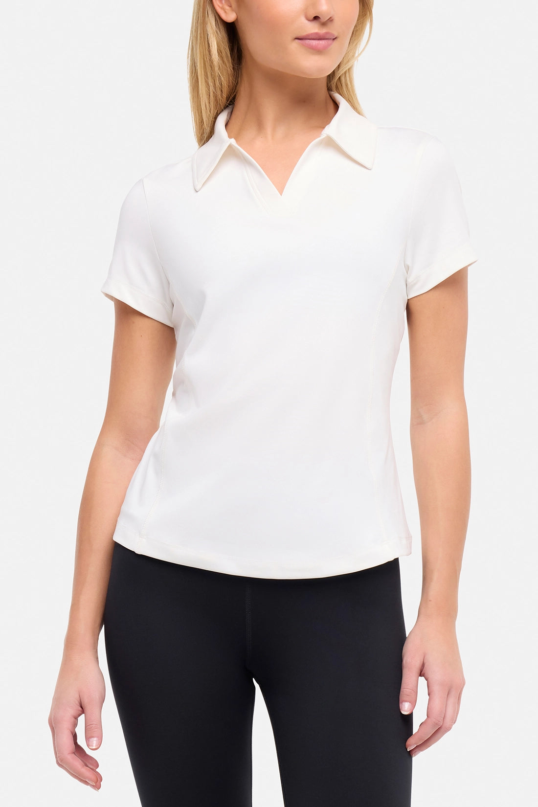 Front view of woman wearing a white short-sleeve polo shirt and black pants on a plain background.