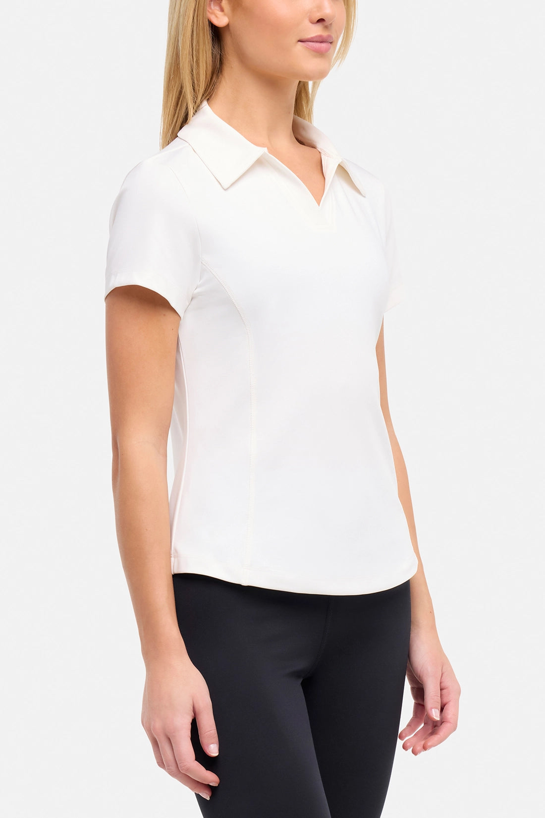 Side view of woman wearing a white short-sleeve polo shirt and black pants on a plain background.