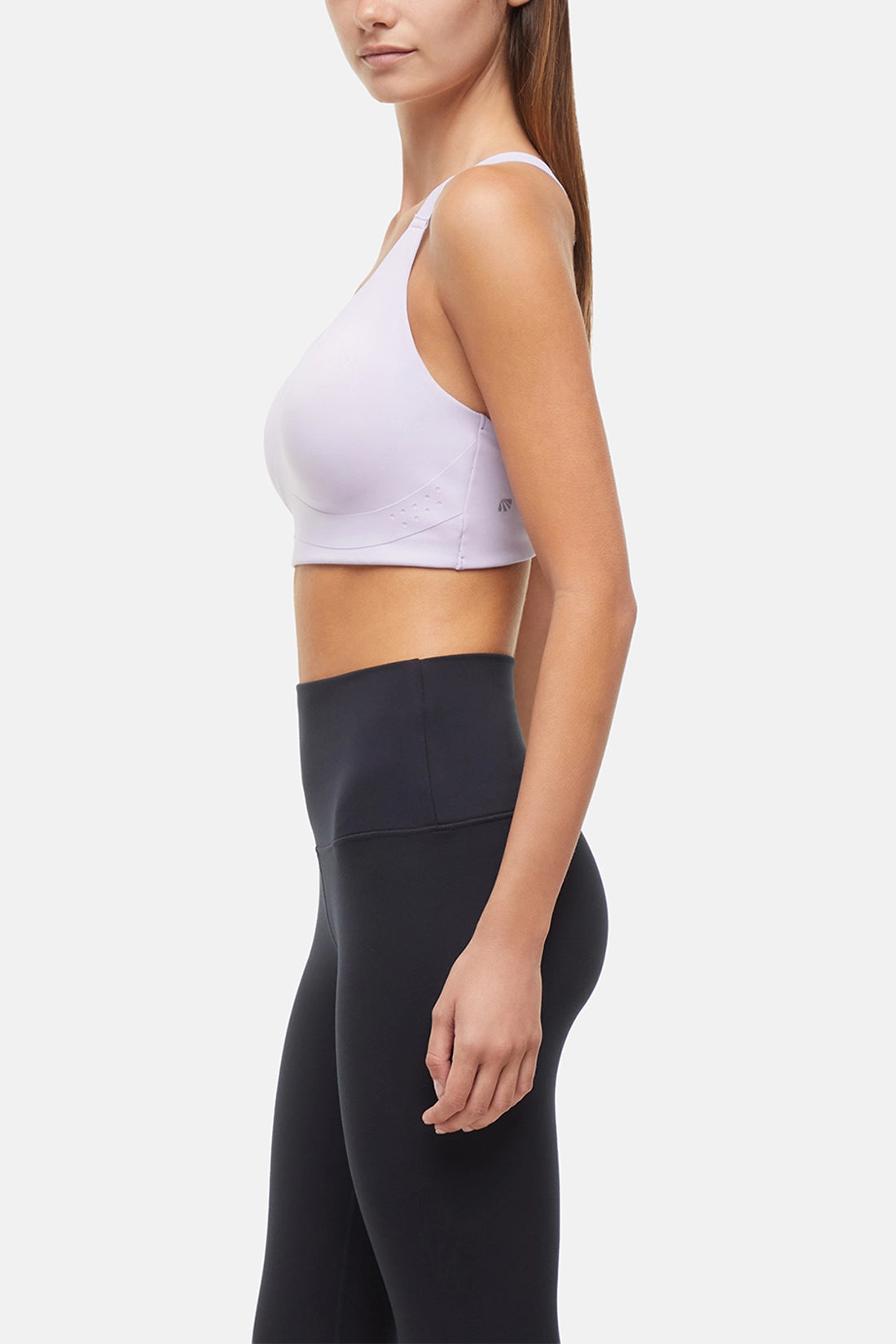 Side view of woman wearing a lilac sports bra and black leggings on a light gray background.