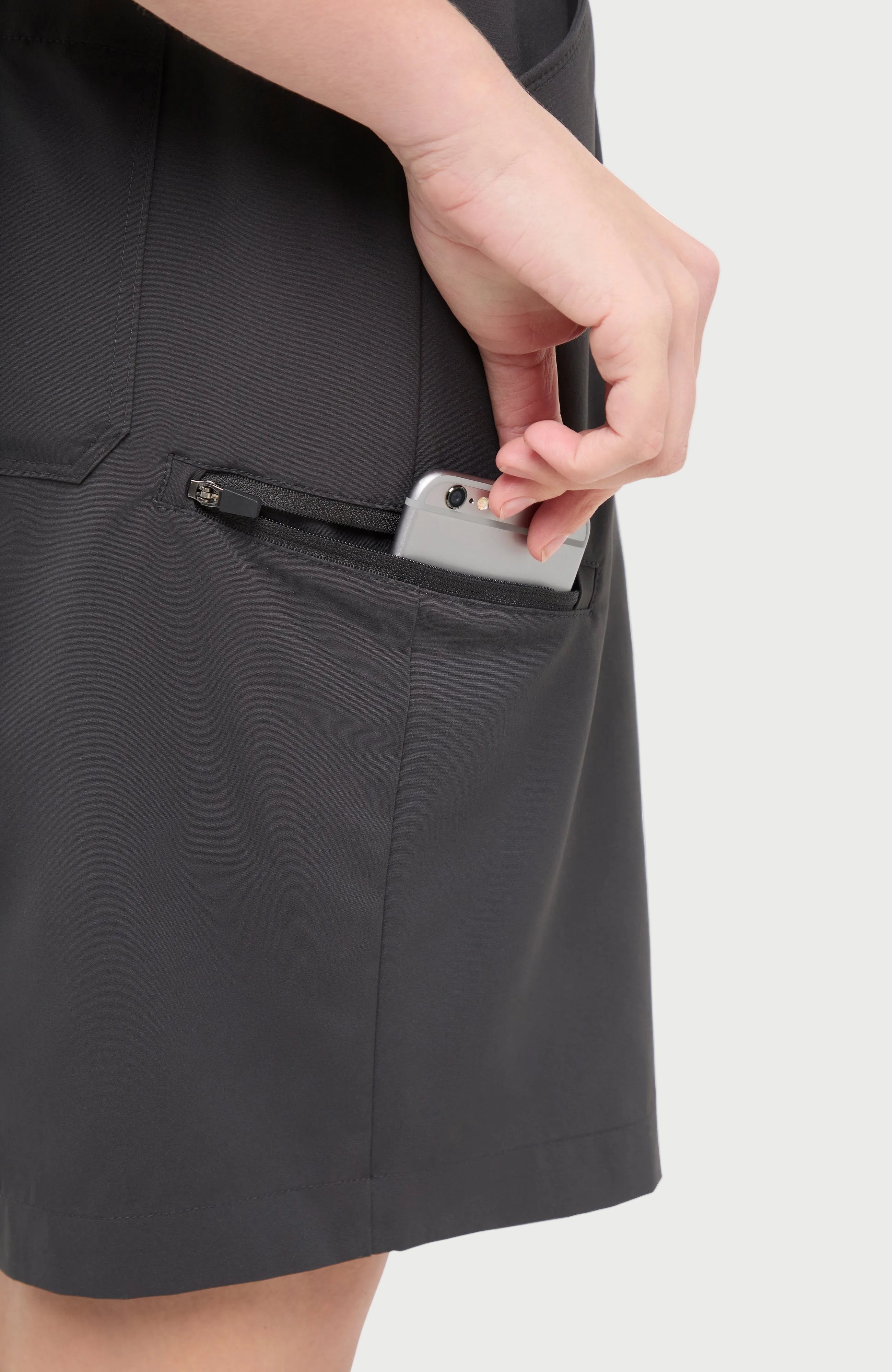 Close up side view of woman wearing dark gray shorts with side zipper pocket, standing on a white background.