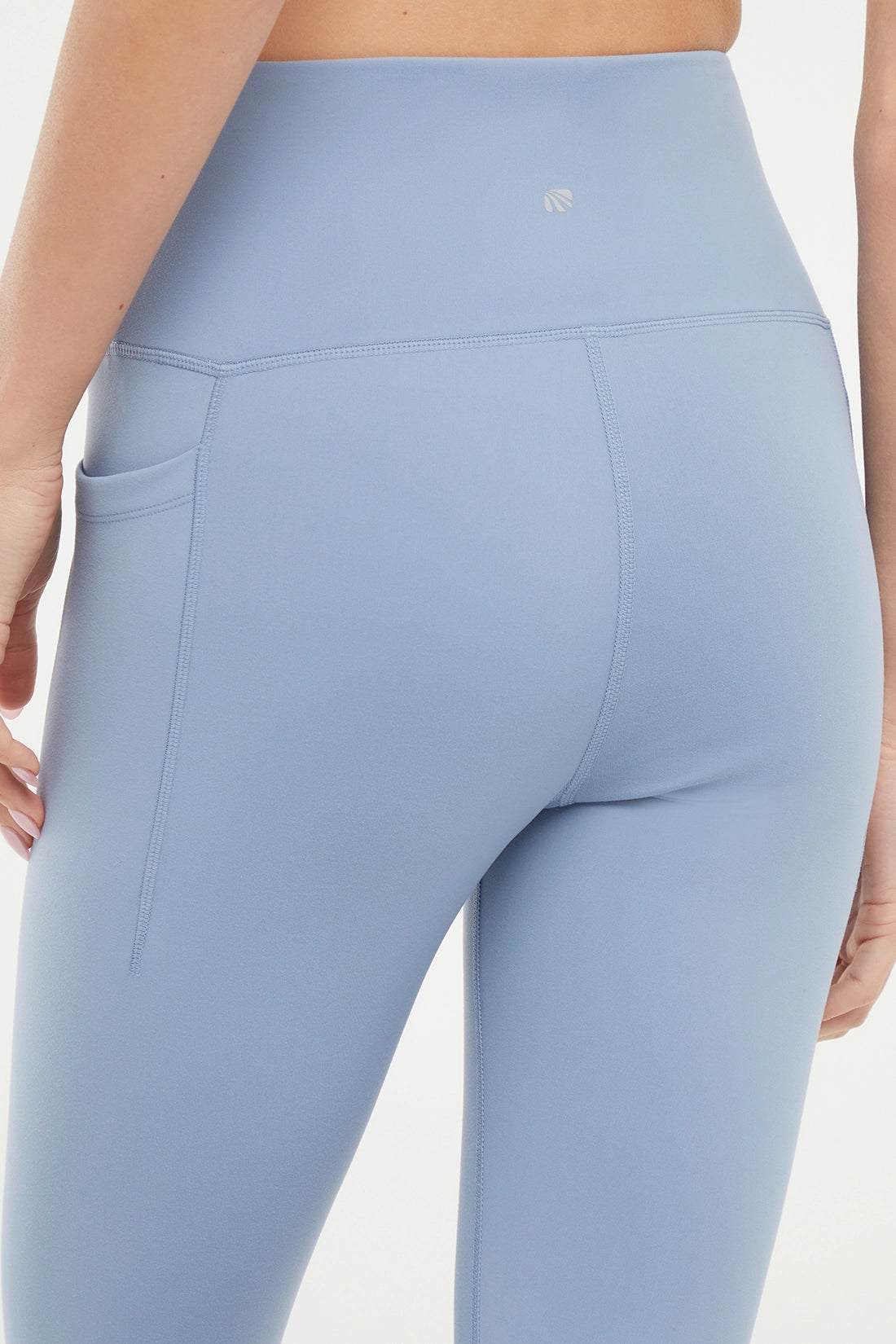 Close up back view of woman wearing light blue leggings worn by a person on a white background.