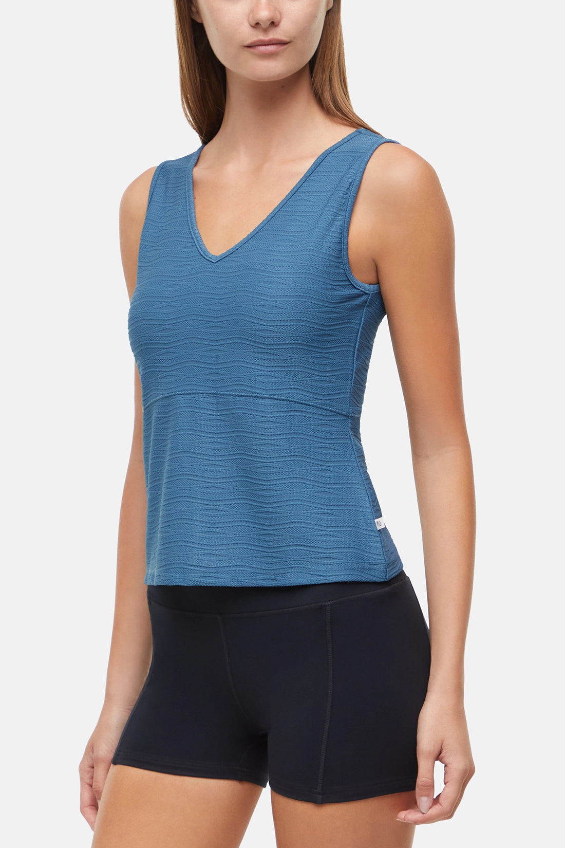 Front view of woman wearing a blue v-neck tank top and black shorts on a white background