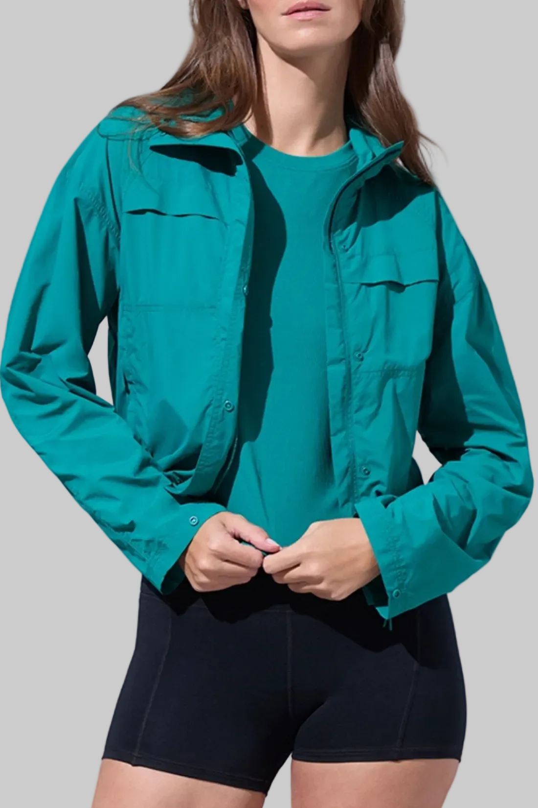 Front view of woman wearing a teal jacket and black shorts on a white background.