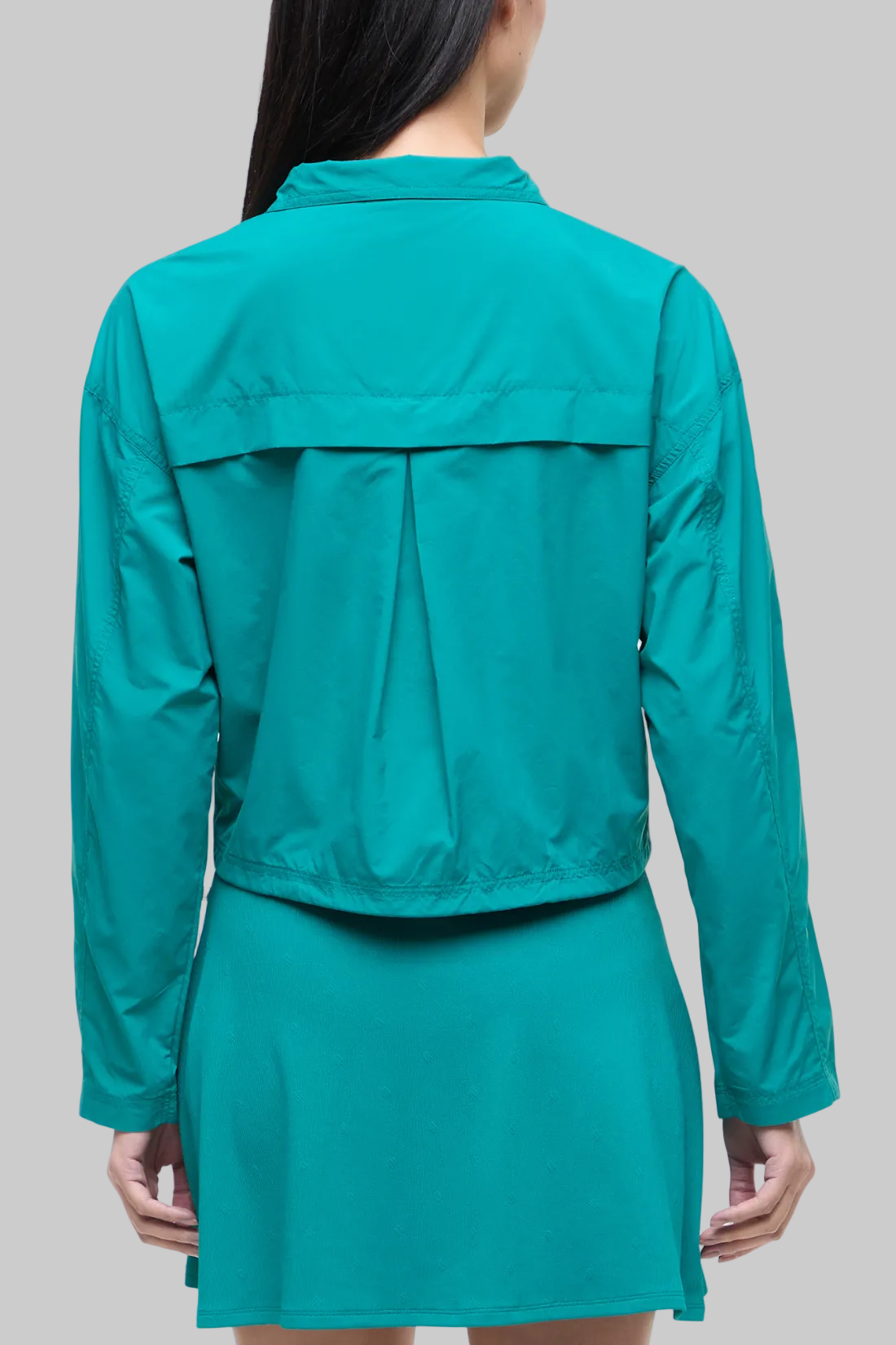 Back view of woman wearing a teal jacket and teal skirt on a white background.