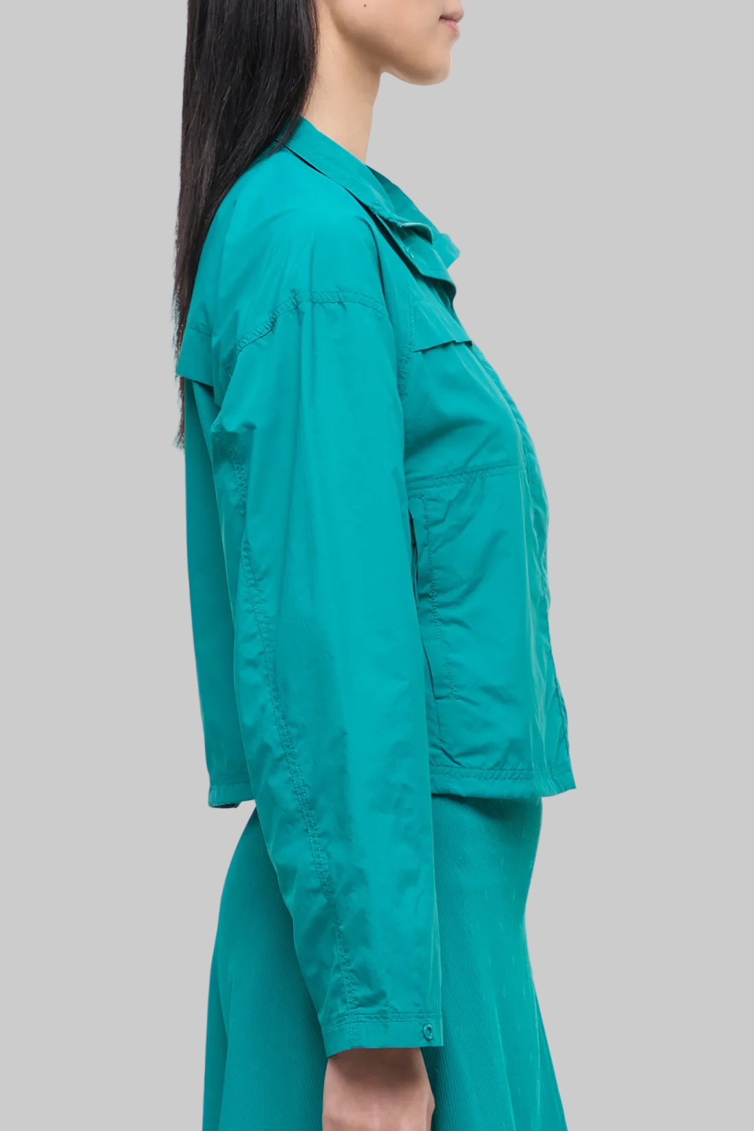 Side view of woman wearing a teal jacket and skirt on a white background.