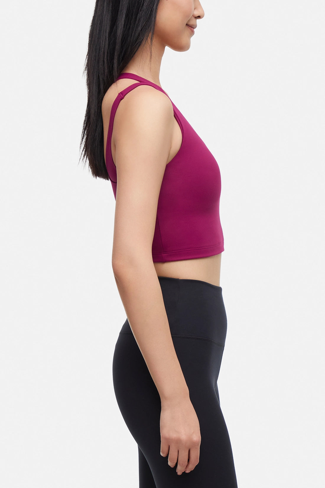 Side view of woman wearing a bright burgundy sports bra and black leggings on a white background.