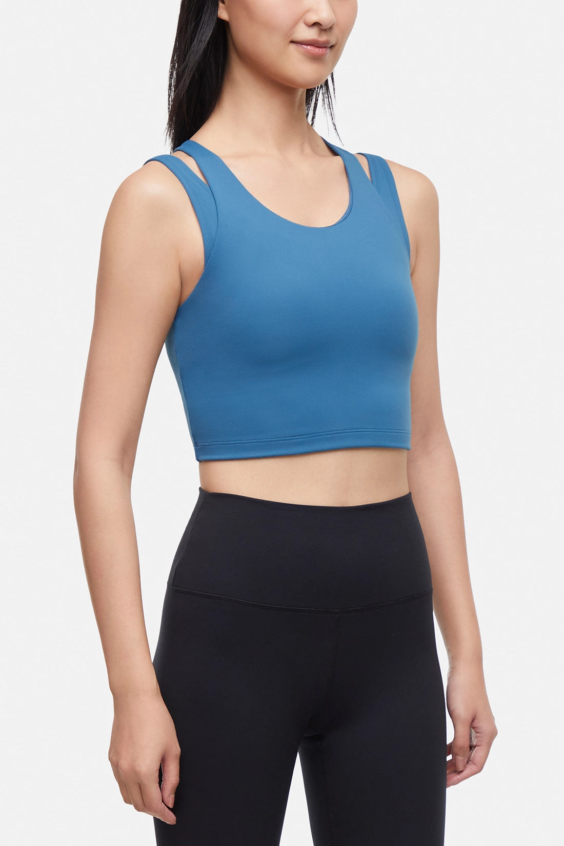 Front view of woman wearing a blue sports bra and black leggings on a white background.