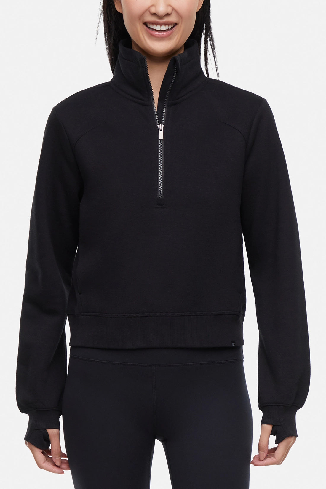 Front view of woman wearing black half-zip pullover with thumbholes on a white background.