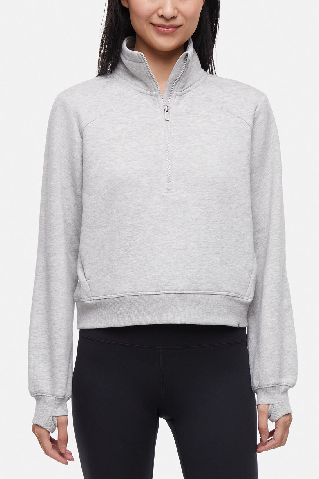 Front view of woman wearing heather gray half-zip pullover with thumbholes on a white background.