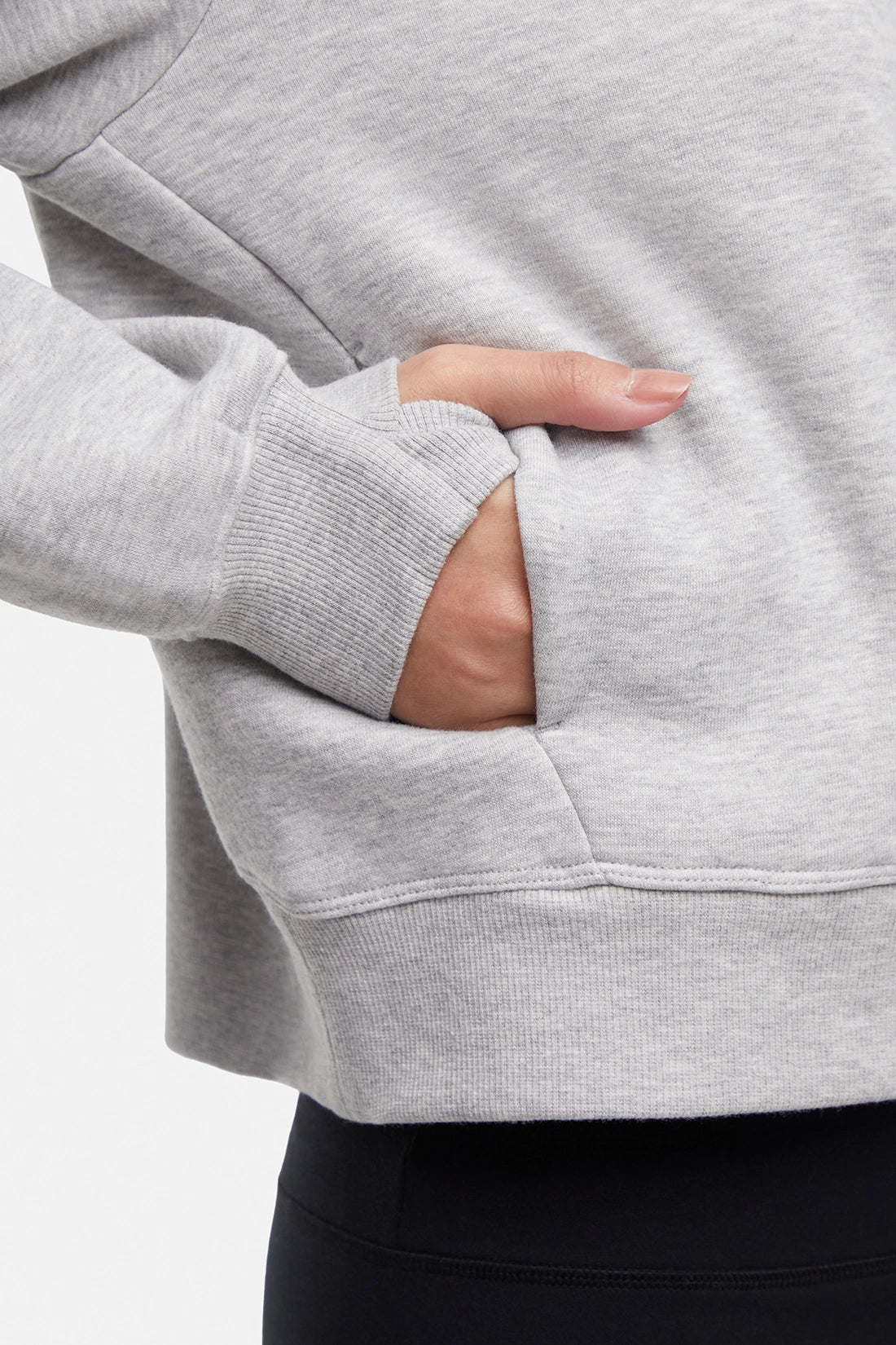 Close up view of woman wearing heather gray half-zip pullover with thumbholes on a white background.