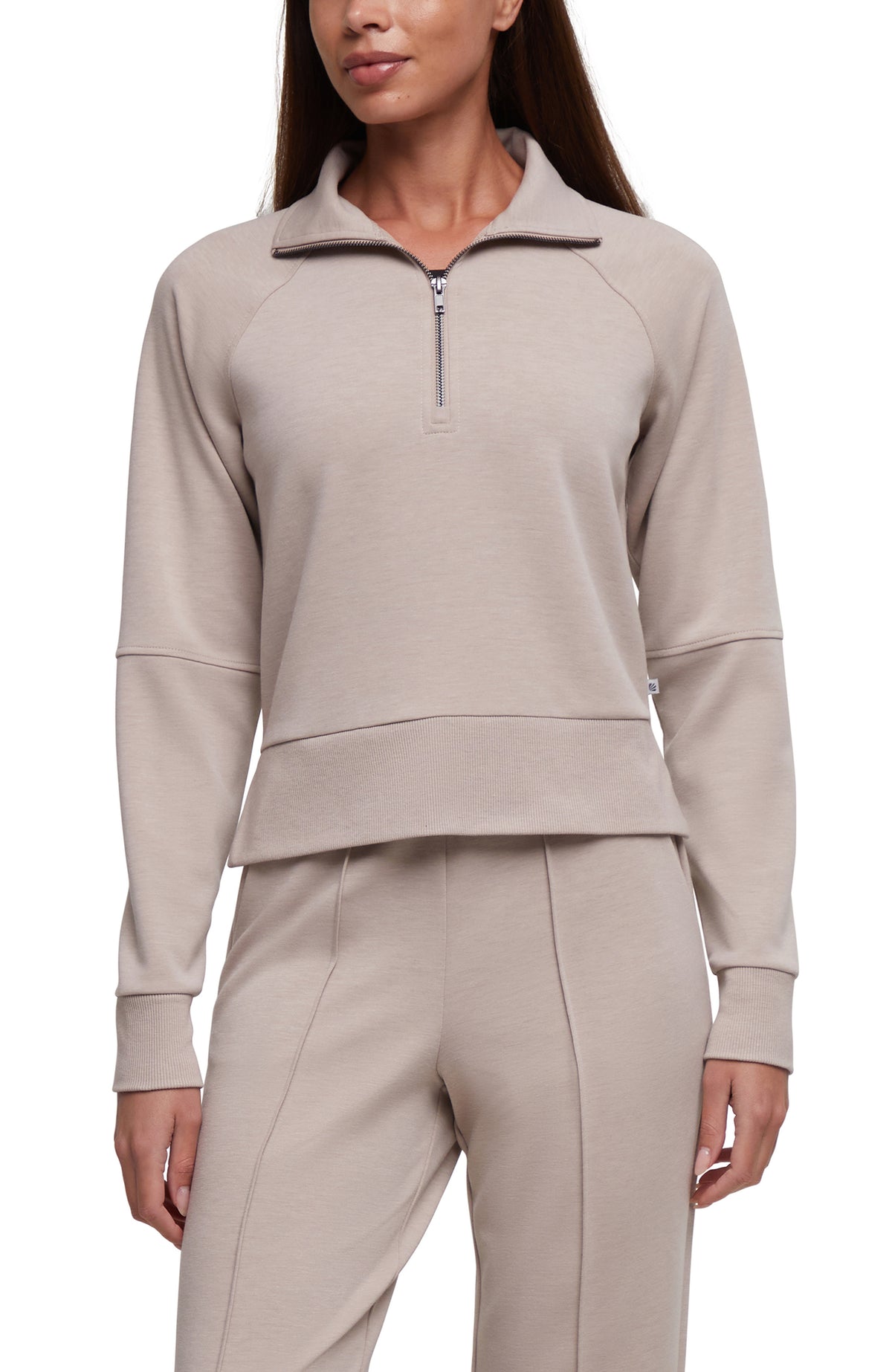 A woman wearing a light taupe-beige long-sleeve quarter-zip sweatshirt and matching pants against a plain white background.