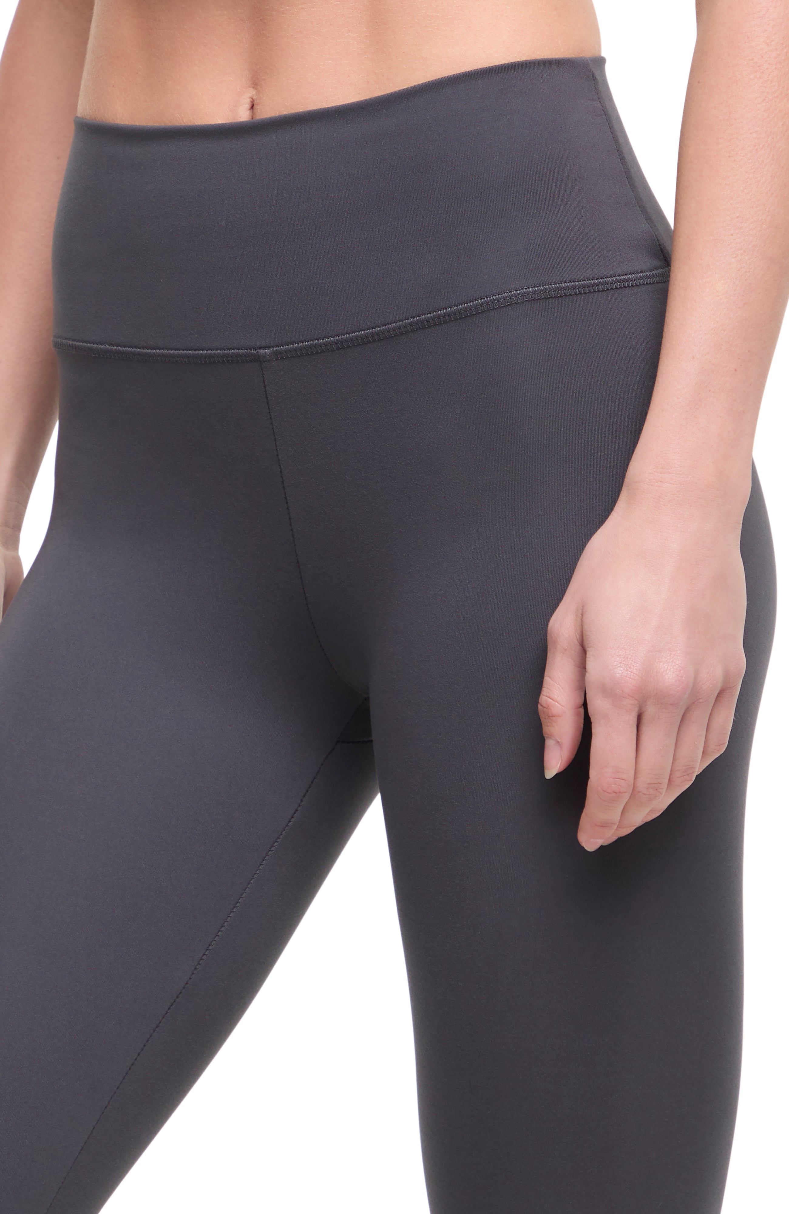 Close up front view of woman wearing dark gray leggings with a white background.