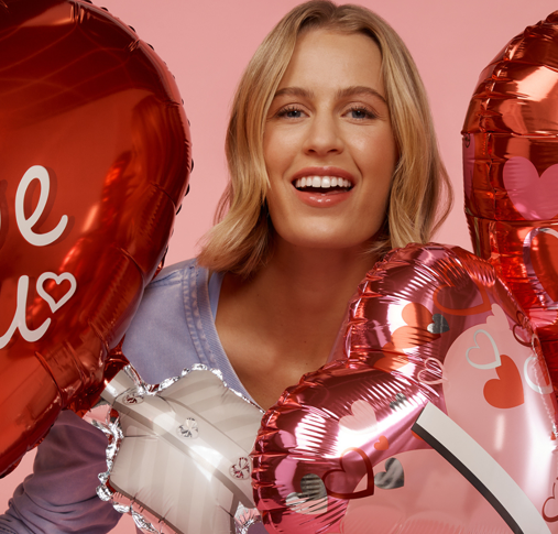 Smiling blonde woman with heart-shaped balloons against a pink background, radiating joy and love—perfect for Valentine's Day and celebration themes