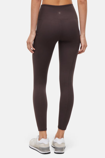 Back view of woman wearing dark brown leggings with a white background. 