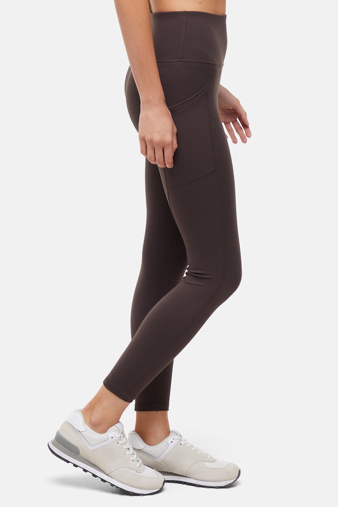 Side view of woman wearing dark brown leggings with a white background. 
