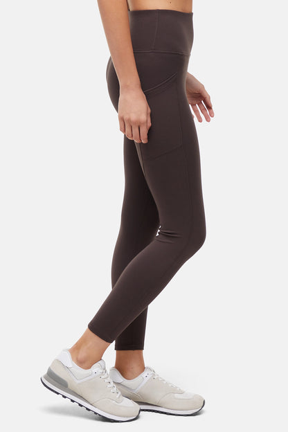 Side view of woman wearing dark brown leggings with a white background. 