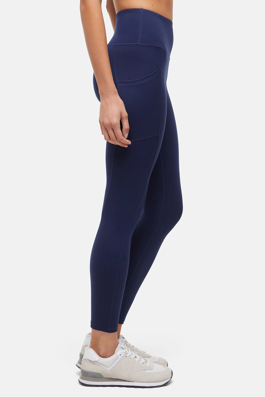 Side view of woman wearing navy leggings with a white background. 