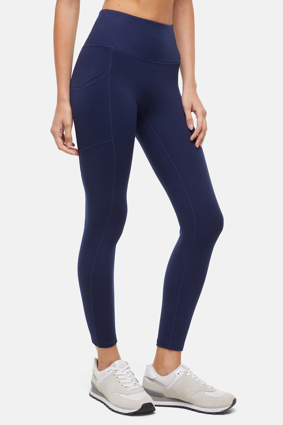 Side view of woman wearing navy leggings with a white background. 