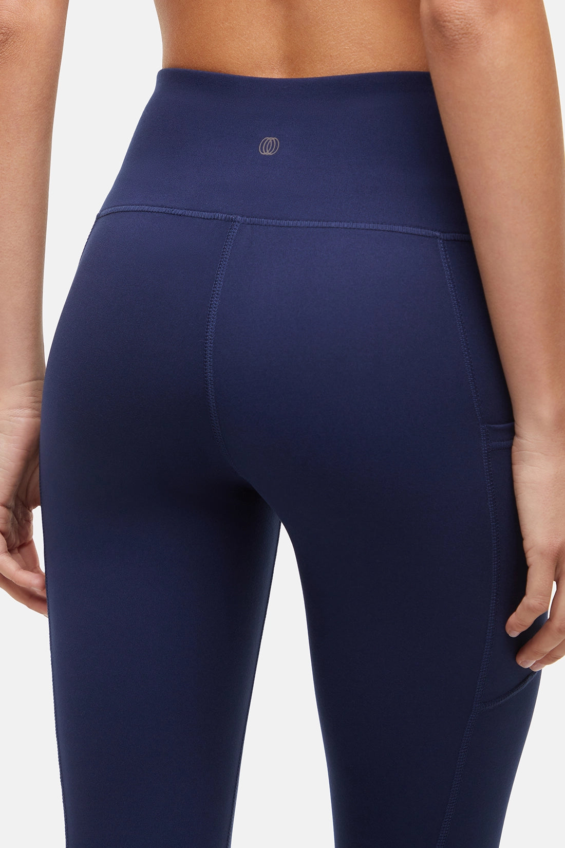 Close up back view of woman wearing navy blue leggings with a white background. 