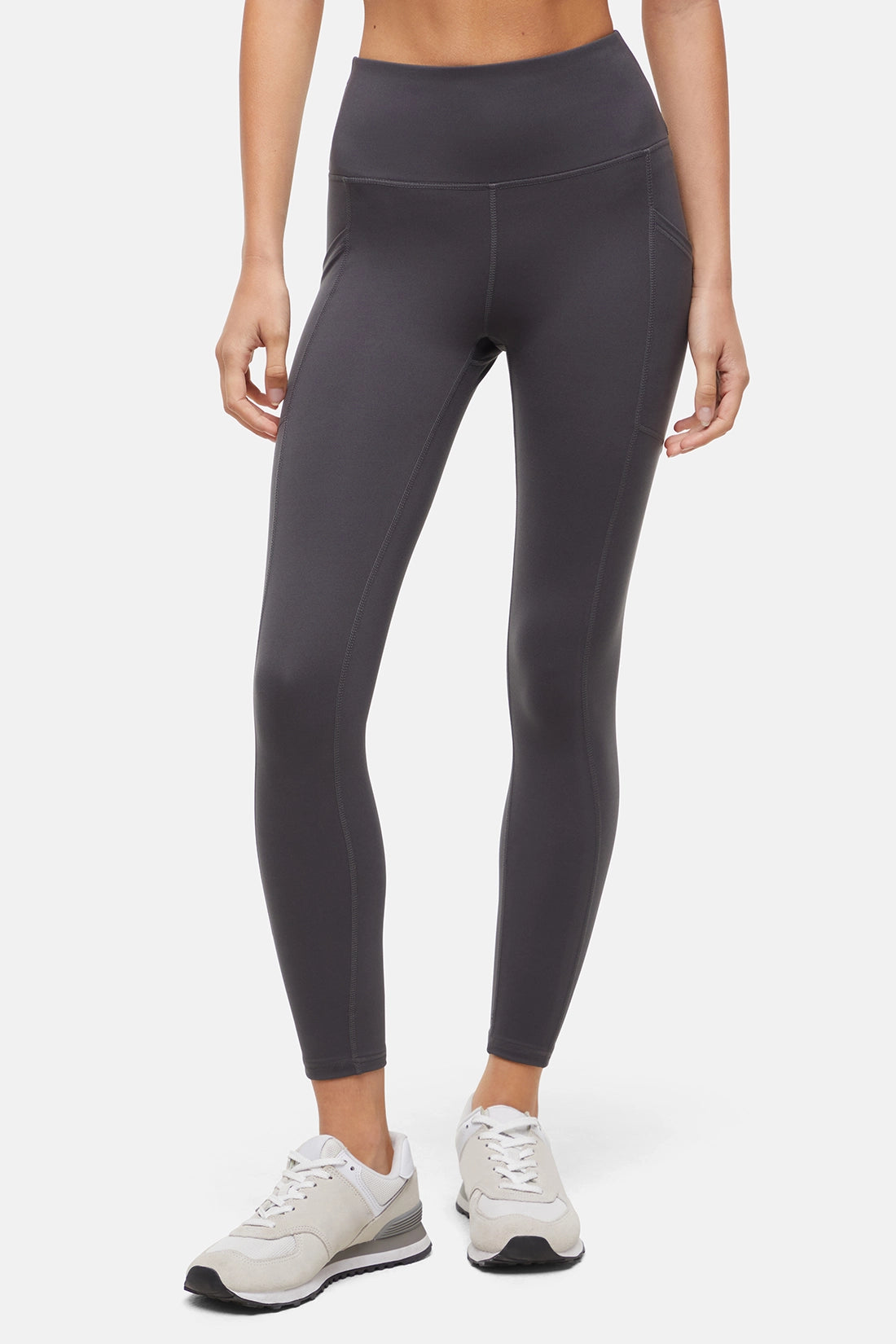 Front view of woman wearing dark gray leggings with a white background. 