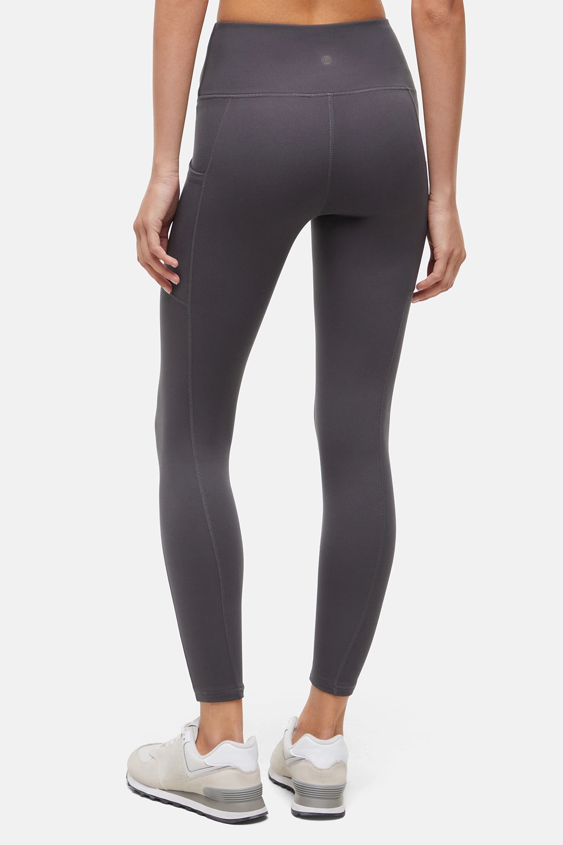 Back view of woman wearing dark gray leggings with a white background. 
