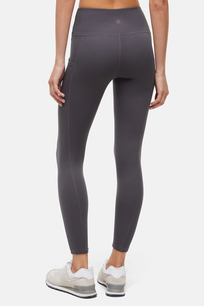 Back view of woman wearing dark gray leggings with a white background. 